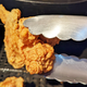 fried chicken wing held by tongs